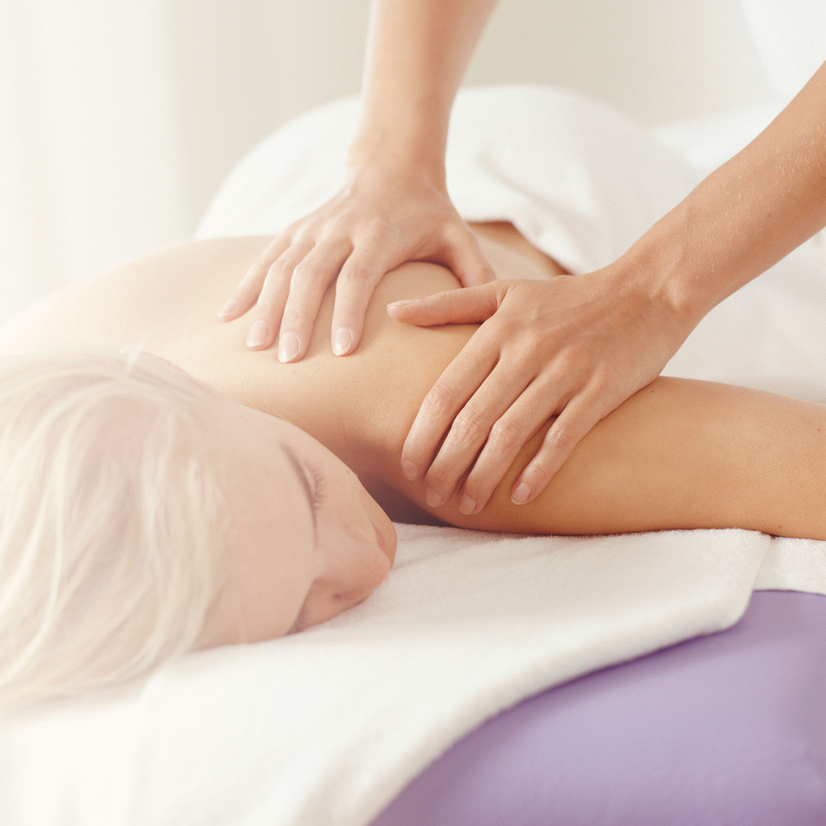 woman laying face down getting a massage with someone's hands on her sholder
